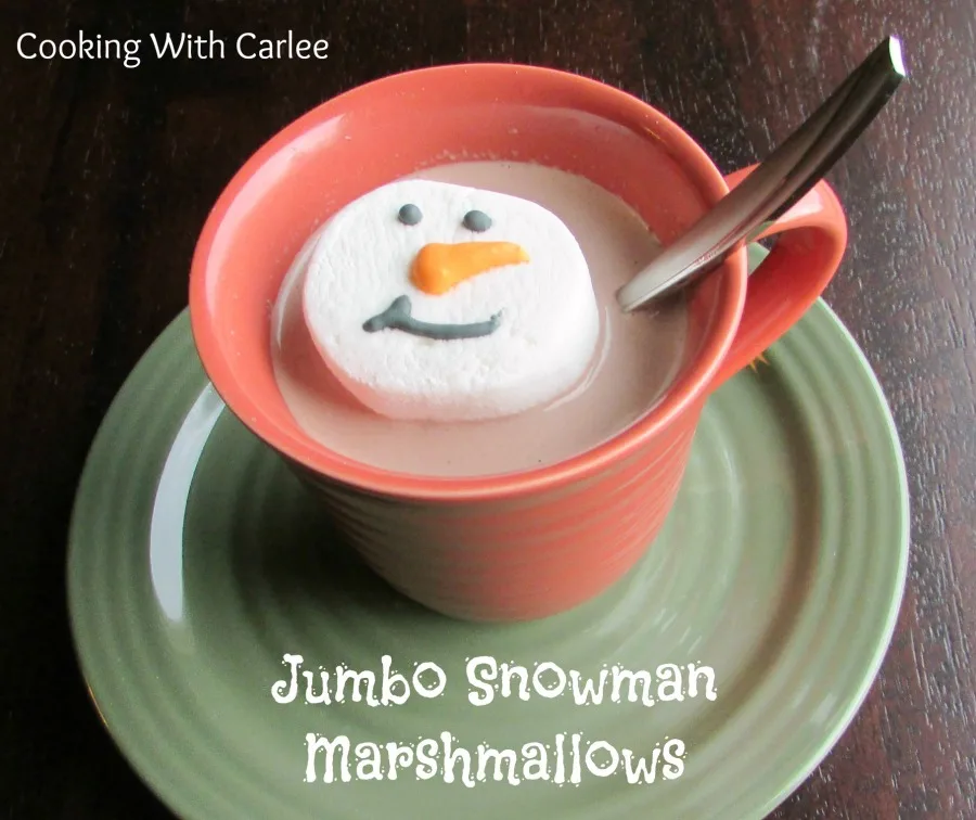 mug of hot chocolate with large marshmallow decorated like snowman head on top.