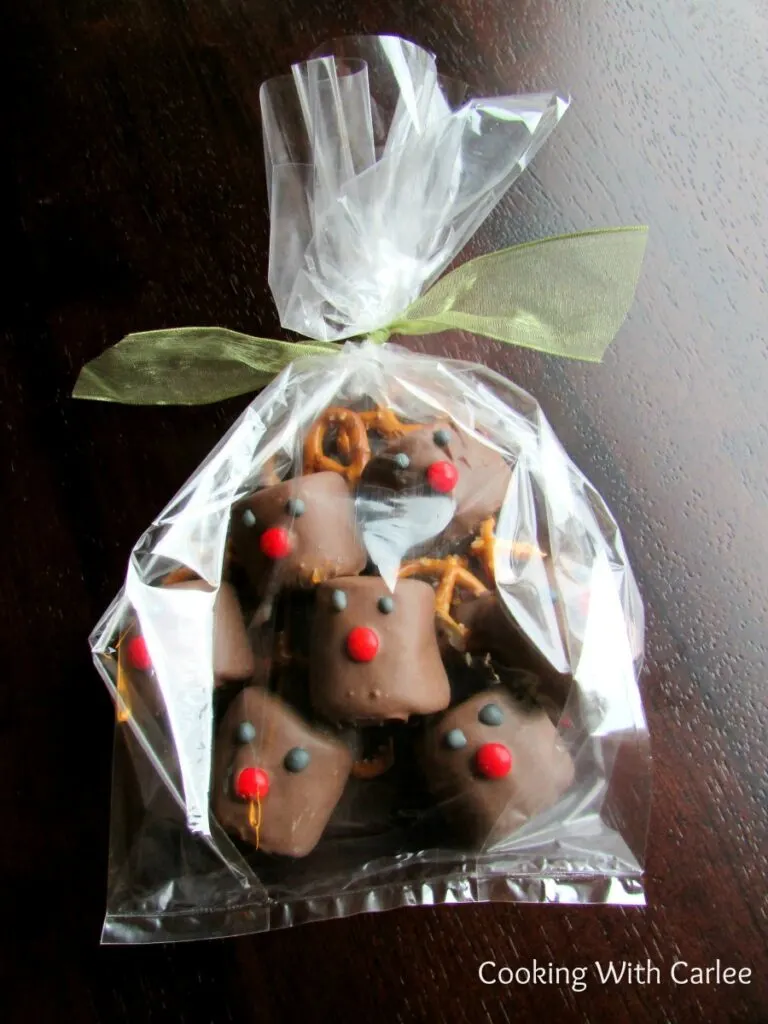 Cellophane bag filled with chocolate dipped marshmallows decorated to look like rudolph the red nosed reindeer tied with a bow ready to be gifted.