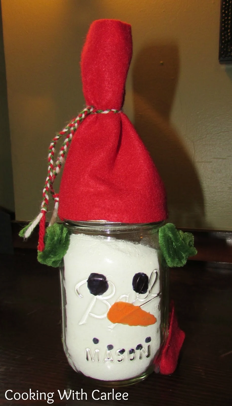 Ball jar filled with white hot chocolate mix, with snowman face painted on it and felt hat and scarf. 