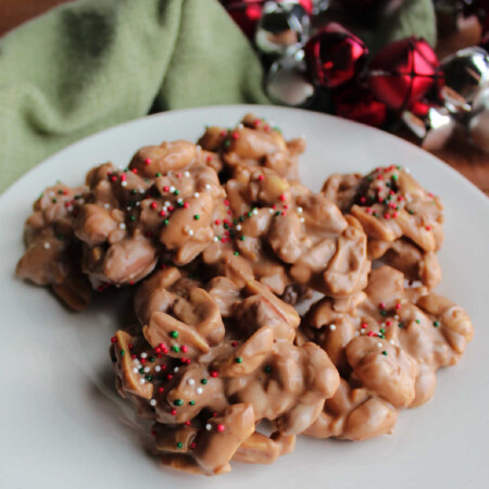 Easy Crockpot Peanut Clusters 1 Chocolate peanut clusters topped with Christmas sprinkles on plate, ready to eat.