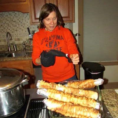 MiMi standing by several foil wrapped rolls with cinnamon coated dough wrapped around them to make spirals.