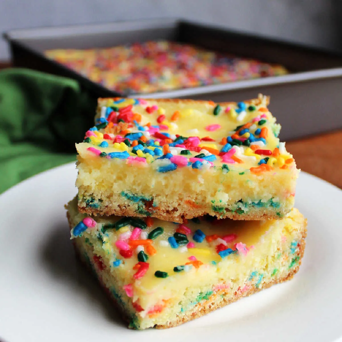 Close up of two pieces of funfetti chess bars with a sprinkle filled cake style crust and gooey cheesecake layer topped with more colorful sprinkles.