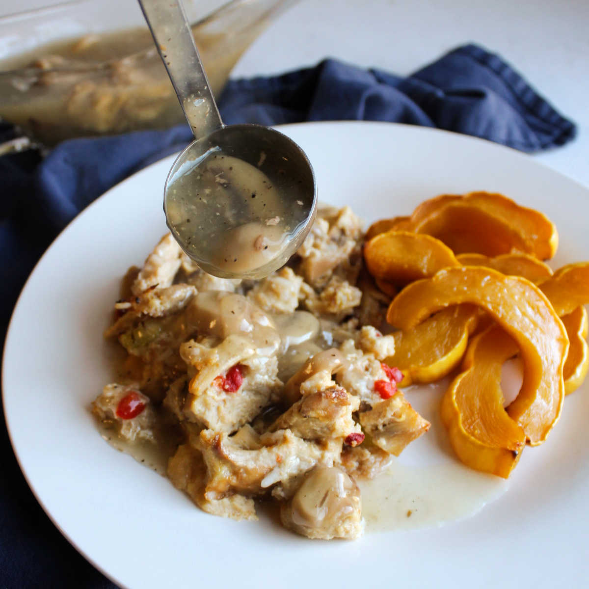 Spooning mushroom gravy over turkey and rice casserole on plate with roasted squash.