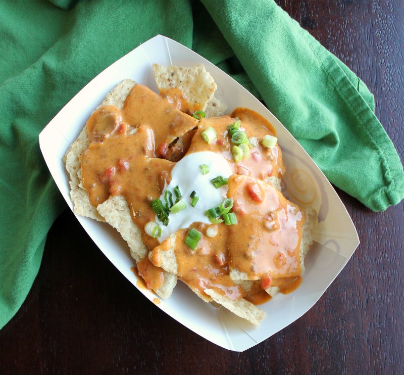 dish of nachos topped with tailgate queso, sour cream and green onions.