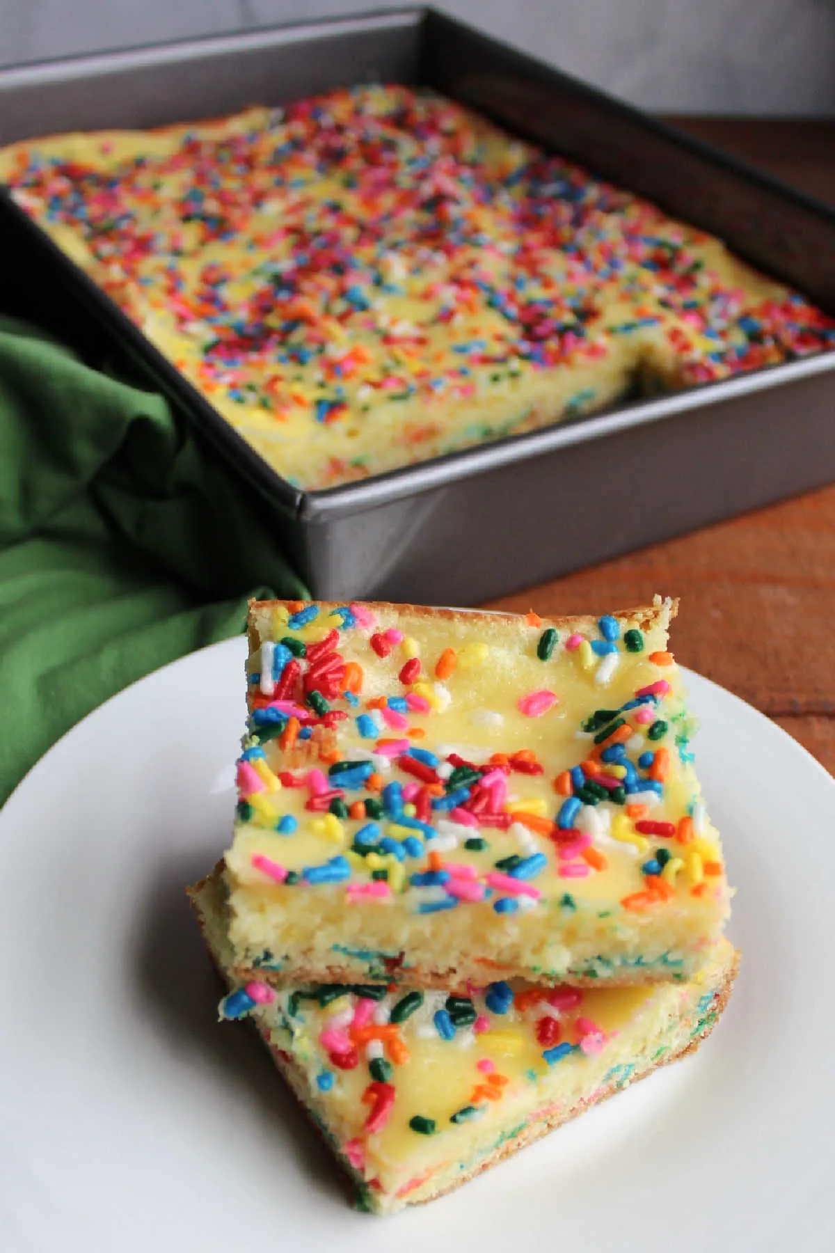 Two pieces of funfetti gooey cake bars stacked in front of pan with remaining cake inside. 