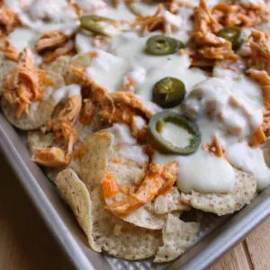 sheet pan full of buffalo chicken nachos with white cheese sauce and jalapenos