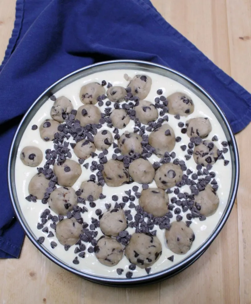 springform pan filled with cheesecake batter, mini chocolate chips and balls of chocolate chip cookie dough.