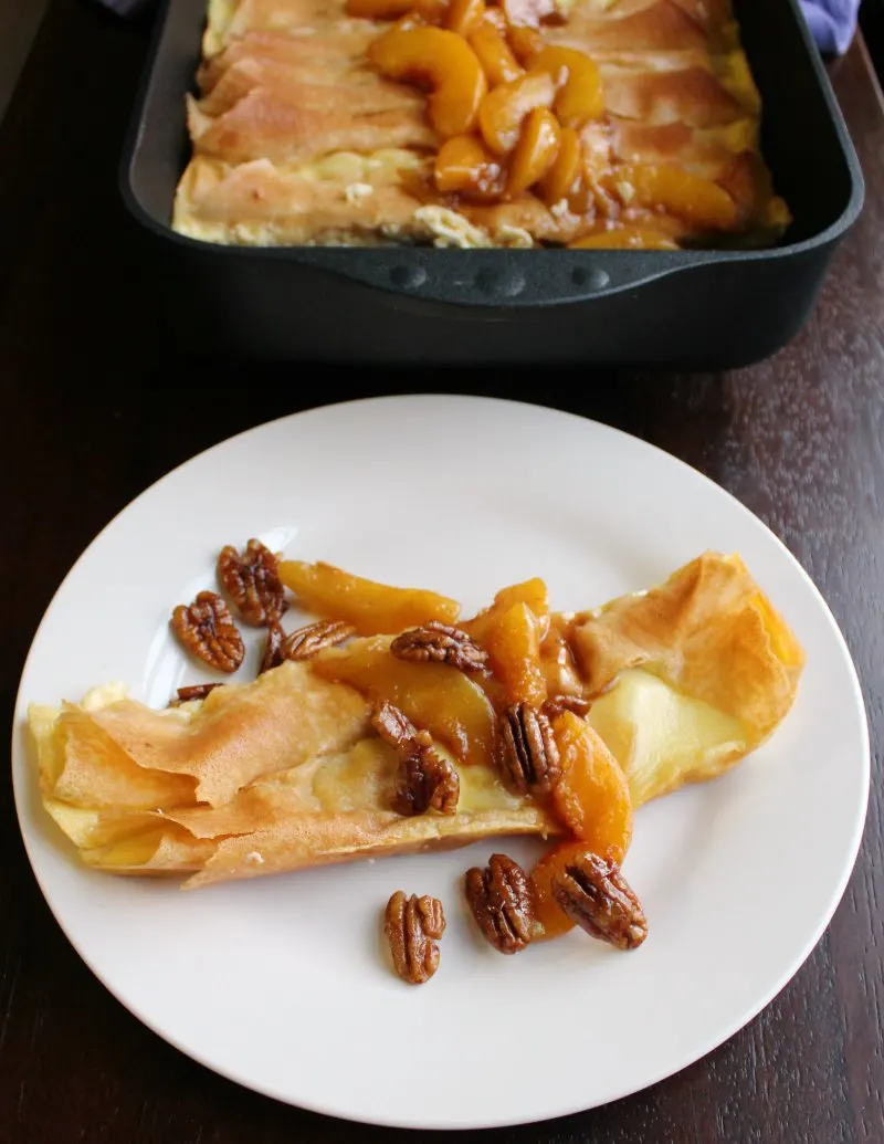 creamy cottage cheese stuffed crepe served with peaches and pecans, remaining batch in pan in background.