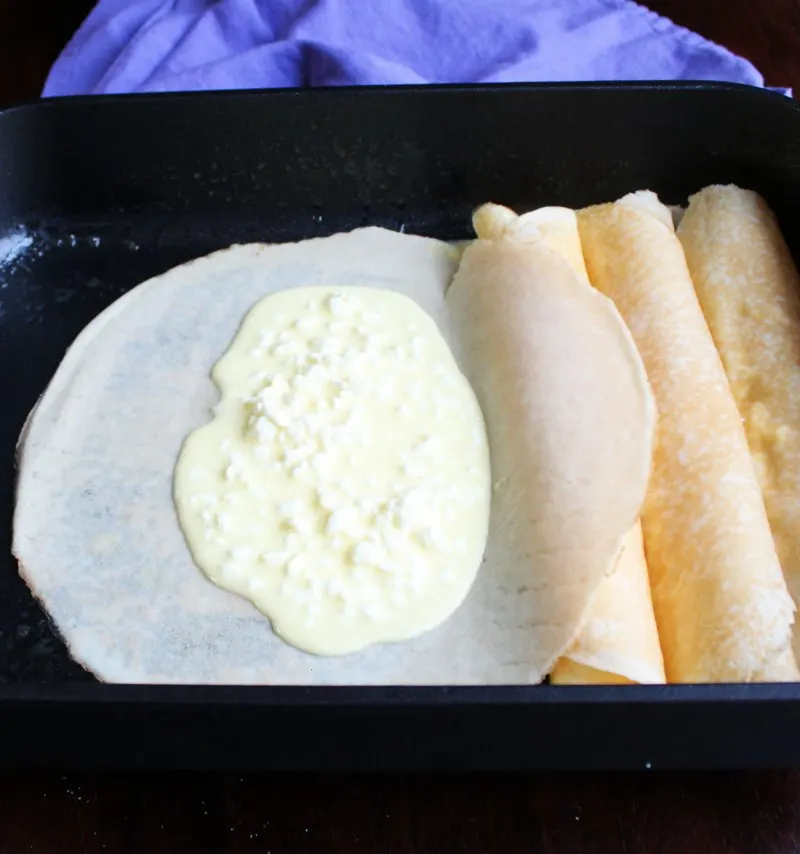 thin crepe in pan with cottage cheese filling in the center, ready to be rolled.