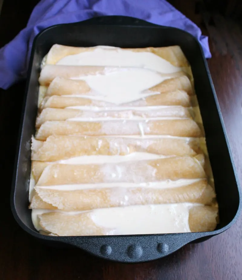 rolled up crepes with cream cheese filling in roasting pan topped with custard sauce ready to bake.