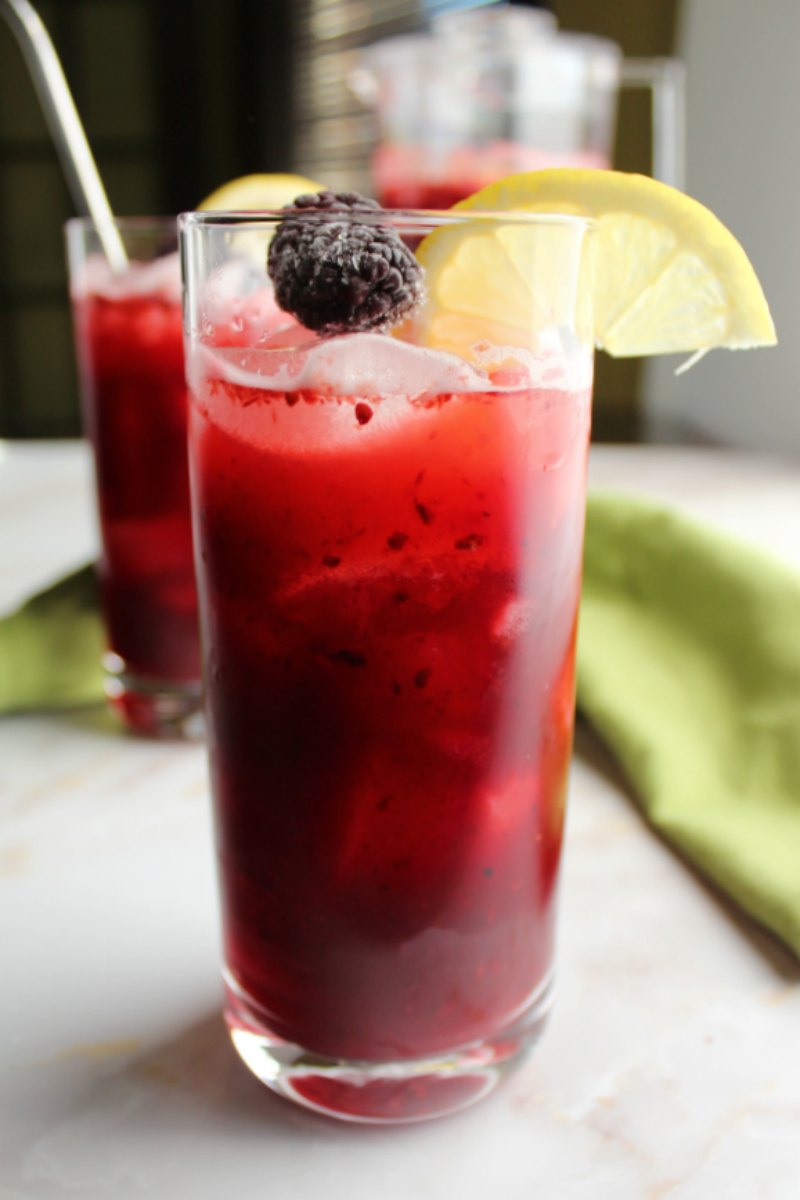 glass of deep purple blackberry lemonade with slice of lemon on the rim, ready to drink.