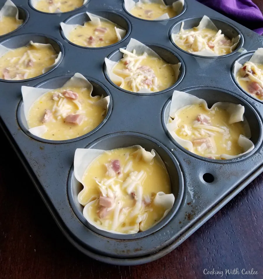 muffin tin lined with wonton wrappers filled with egg, ham and cheese mixture ready to bake.