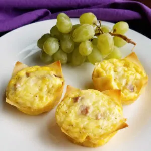 3 mini ham and cheese quiche in wonton wrappers on plate with bunch of grapes.