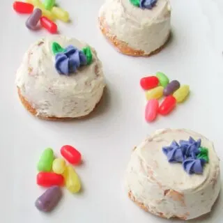 mini angel food cakes with white frosting and sides and purple frosting flowers on top, surrounded with bright colored candy.