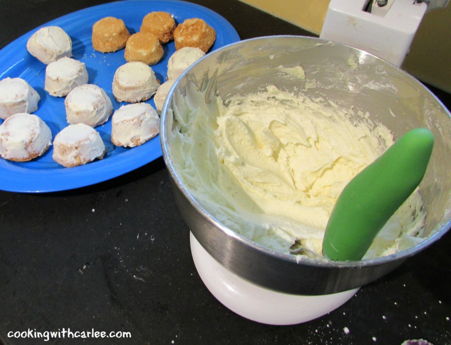 Mixer bowl of sweetened condensed milk buttercream with offset spatula to spread frosting on angel food cupcakes.