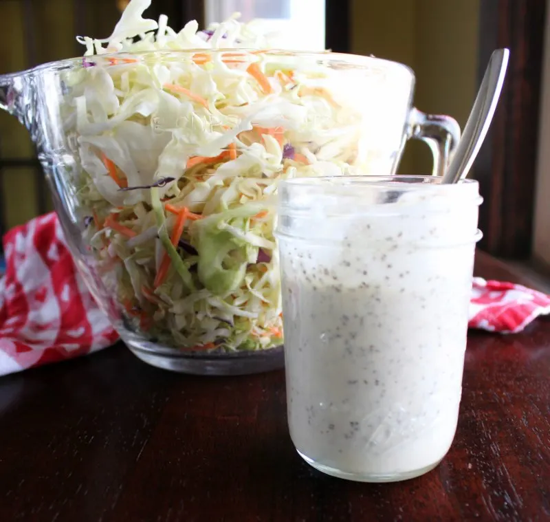 big bowl of shredded cabbage and carrots with a jar of homemade creamy cole slaw dressing.