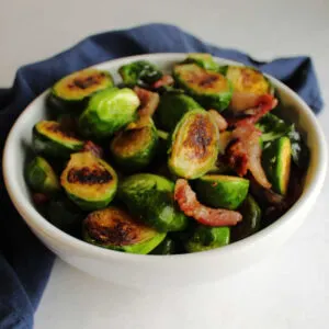 Serving bowl filled with golden brown brussels sprouts halves and bits of bacon.