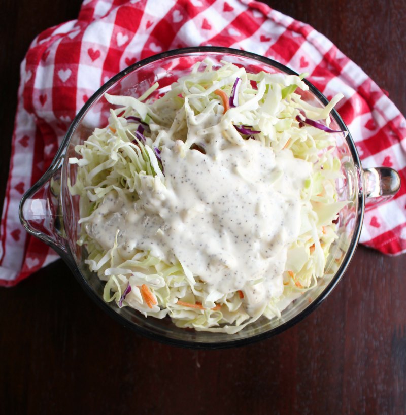bowl of shredded cabbage and carrots with dressing poured over the top