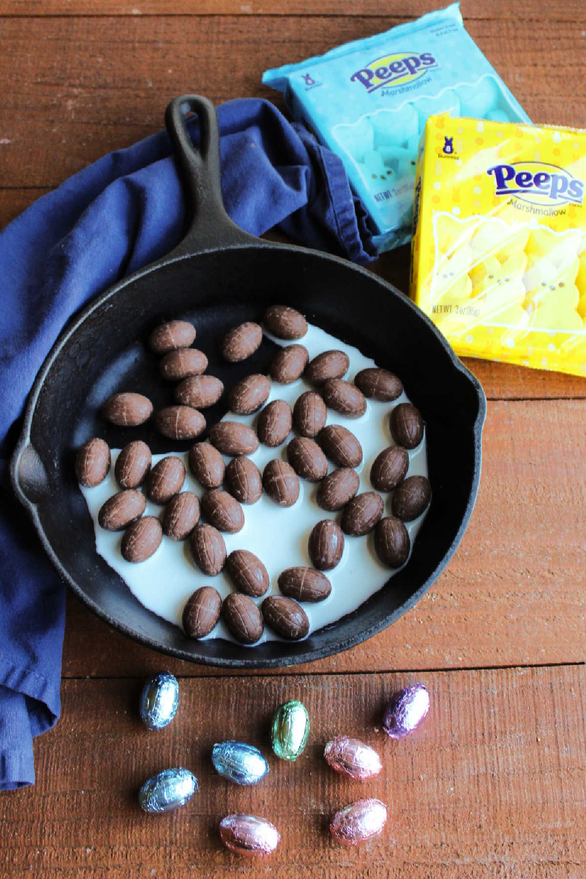 Small chocolate eggs in a pan with some milk next to a couple of packages of bunny shaped Peeps marshmallows.