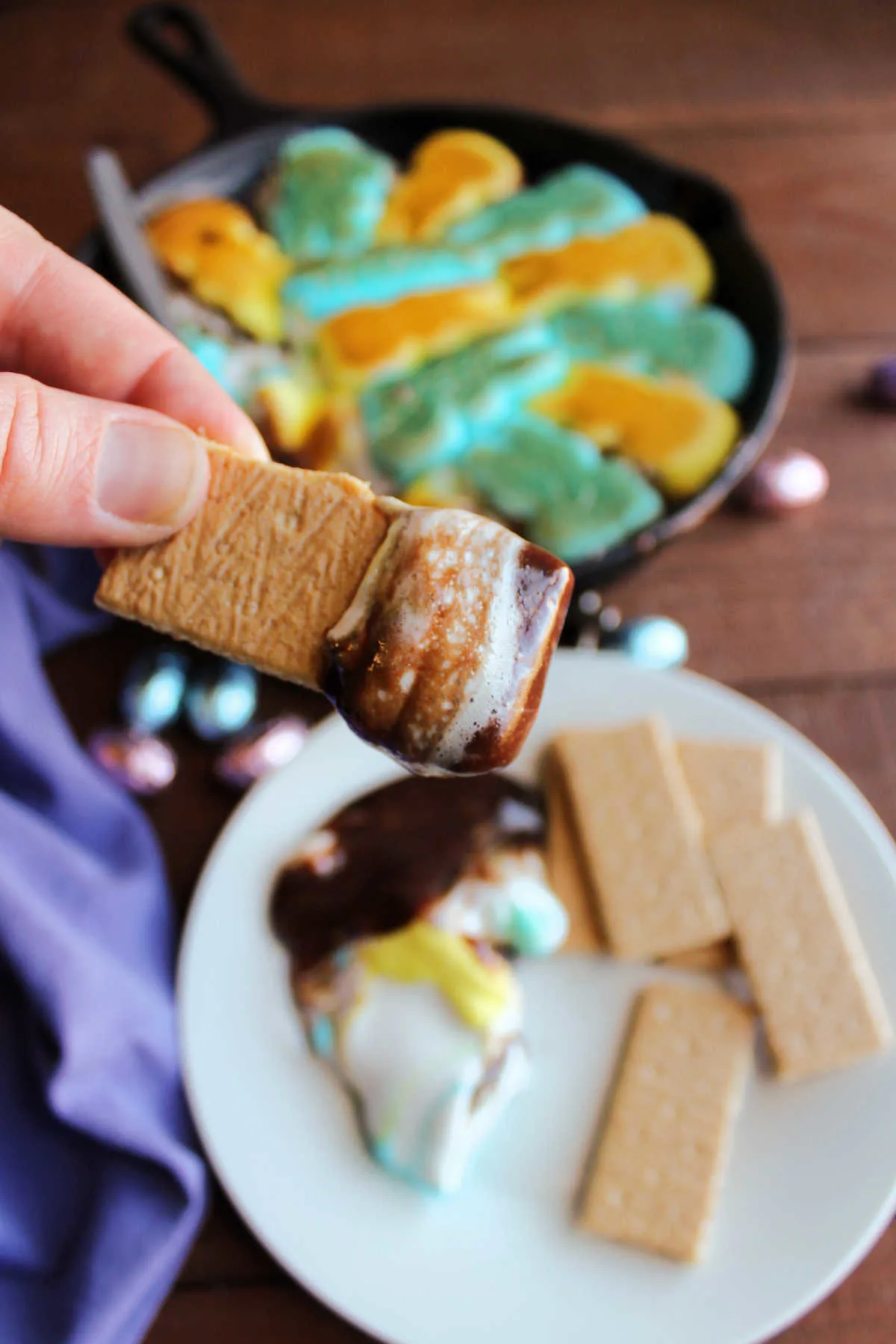 Graham cracker dipped in peeps smore dip showing gooey marshmallow and melted chocolate.