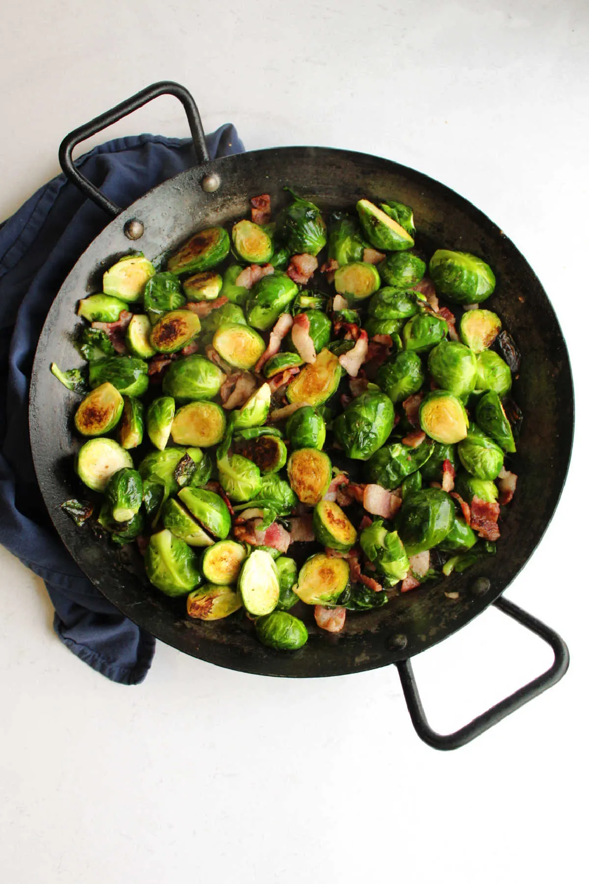 Large black pan filled with roasted brussels sprouts and bacon fresh from the stove.