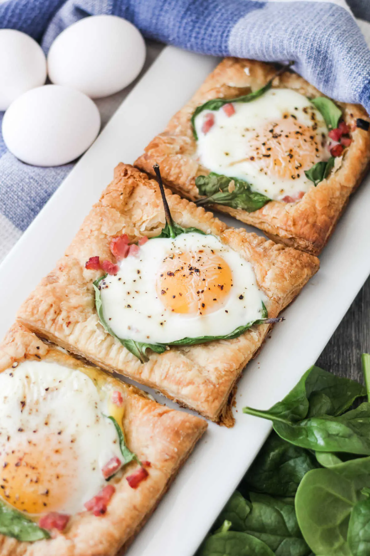 Platter of golden puff pastry squares topped with ham, spinach and eggs baked to perfection.
