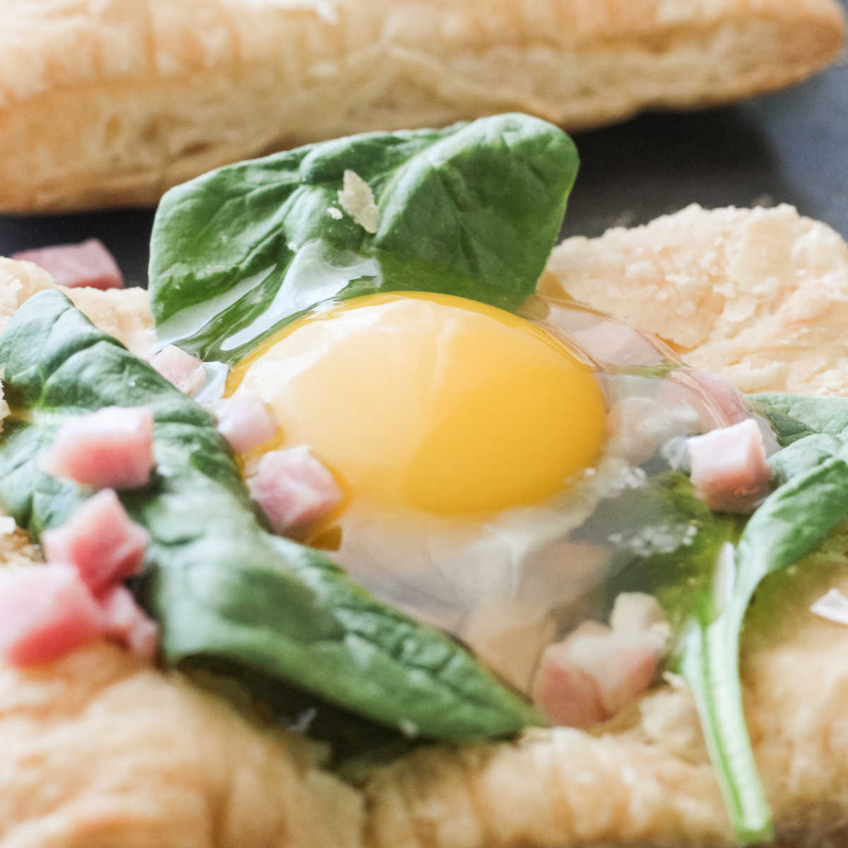 Ham, spinach and raw egg on square of golden puff pastry ready to go back in oven.