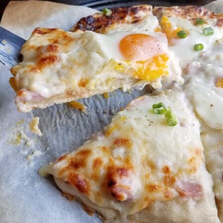 Croque Madame Pizza 4 lifting slice of creamy white pizza with gooey egg on top