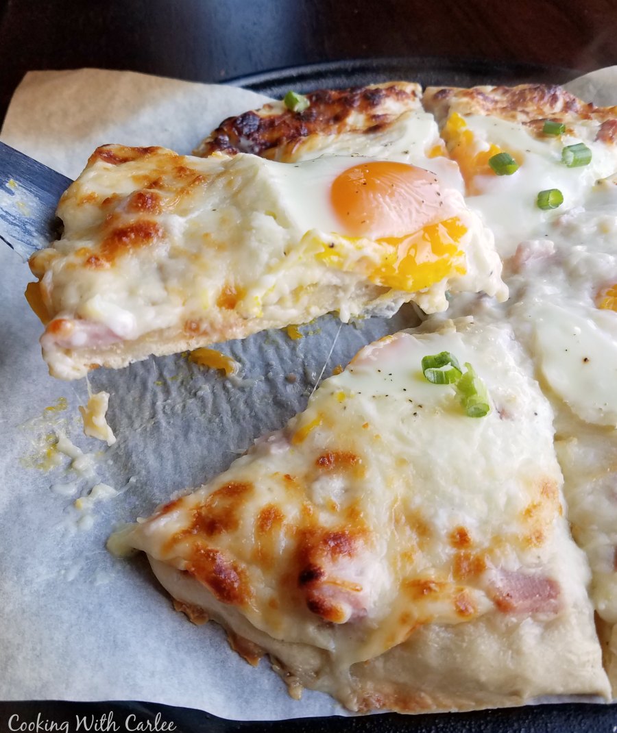 lifting slice of creamy white pizza with gooey egg on top