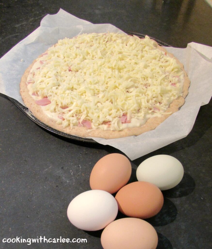 brown eggs next to raw pizza with white sauce, ham and cheese.