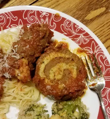Plate with spaghetti, roasted broccoli and slice of braciole with spiral of beef and filling showing.