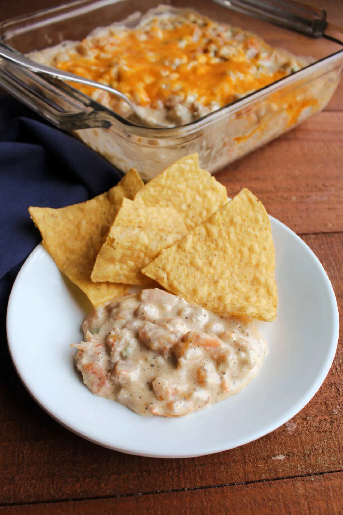 Serving of cheesy cajun shrimp dip on small plate with tortilla chips, ready to eat.