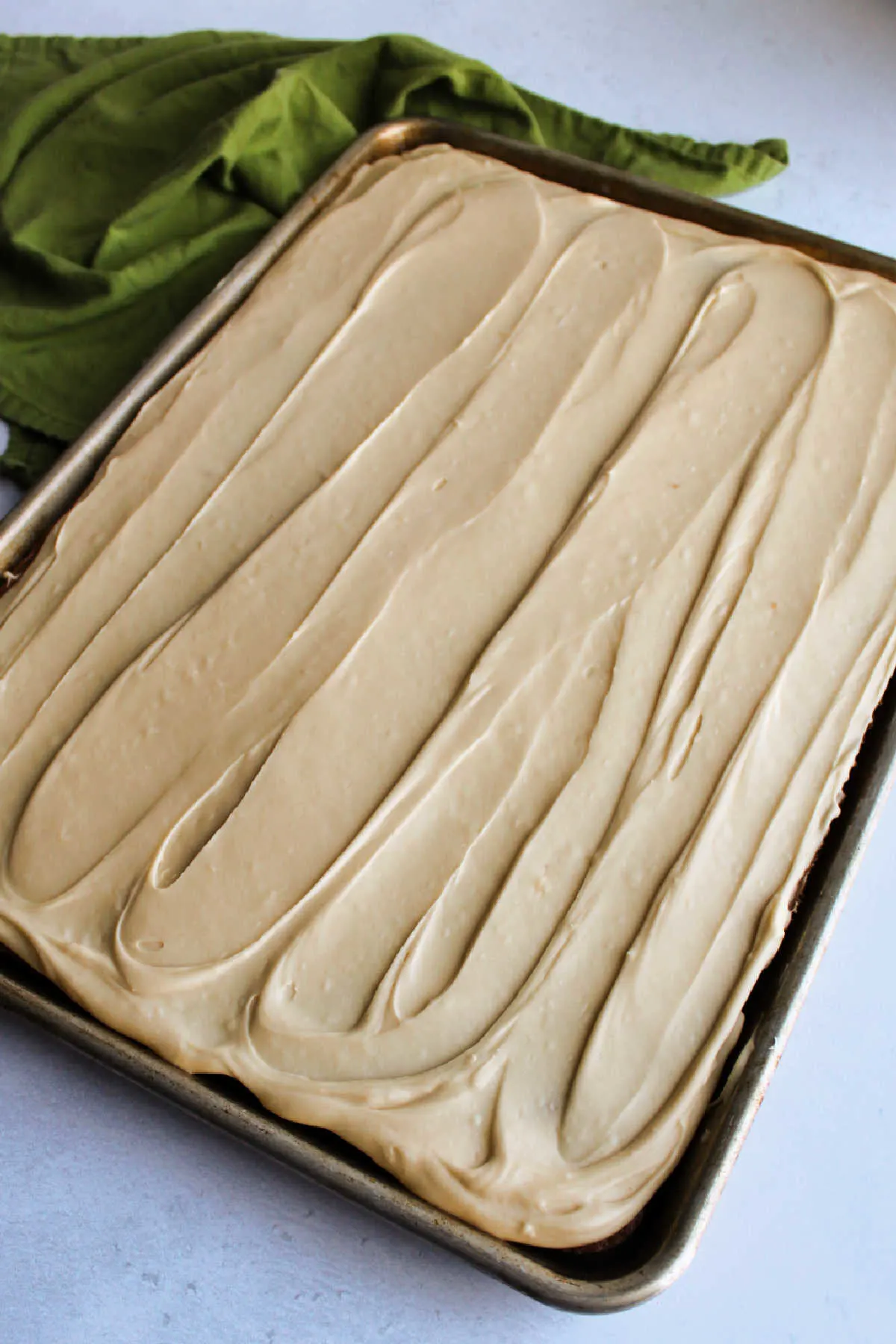 Tan brown sugar icing spread over cake in sheet pan.