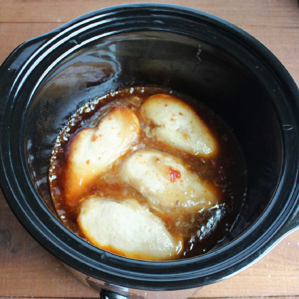 cooked whole chicken breasts in sauce inside crock pot.