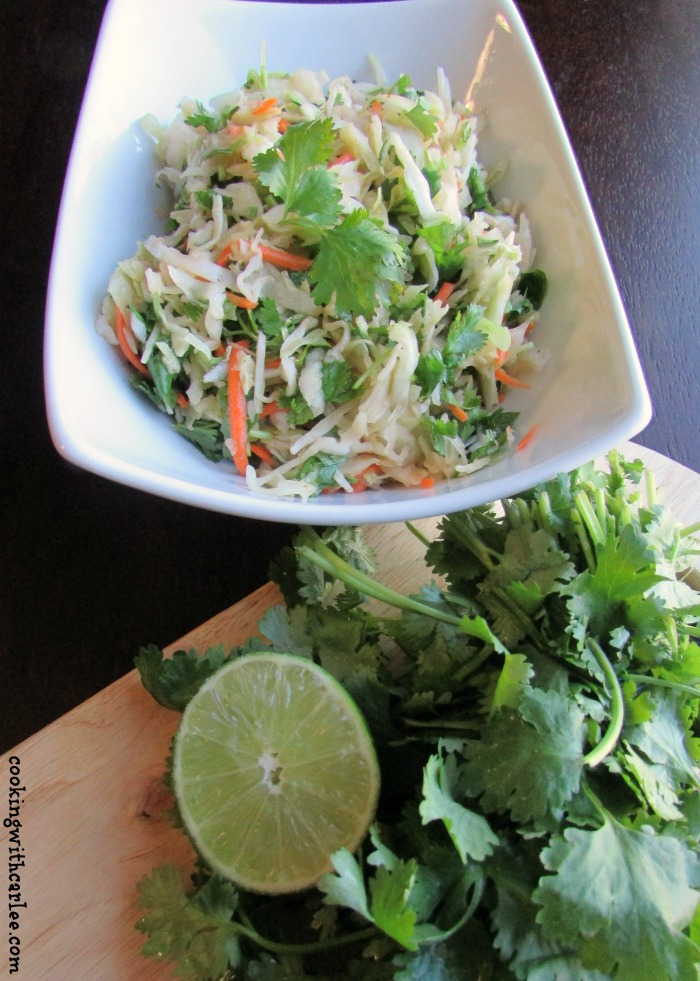 Fresh cilantro and limes next to bowl of honey lime coleslaw, ready to eat.