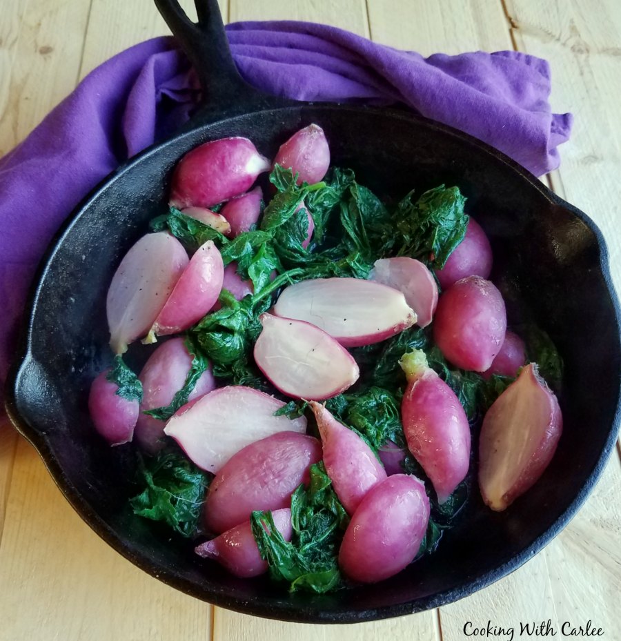 roasted radishes with pink skins and white flesh in cast iron pan surrounded by wilted radish greens.