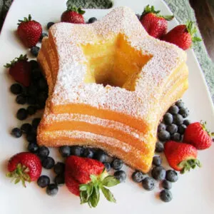 Star shaped sand torte cake dusted with powdered sugar and surrounded with strawberries and blueberries.