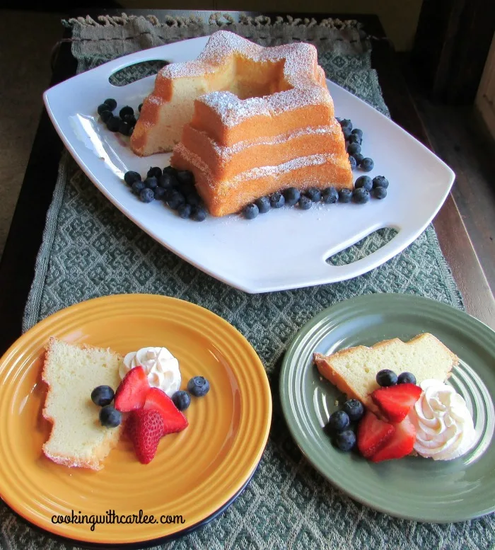 two dessert plates with cake, berries and whipped cream with remaining star shaped cake in background.
