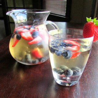 Cup of white sangria with blueberries and strawberries with pitcher in background.