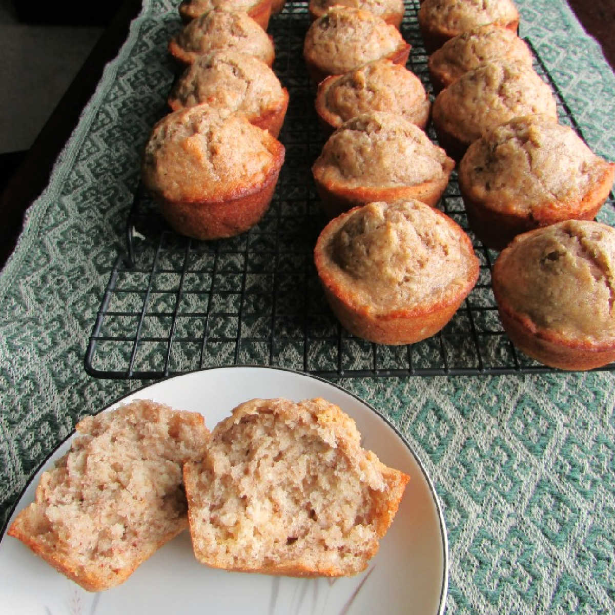 sourdough banana muffin broke in half showing soft center with more muffins on cooling rack in background. 