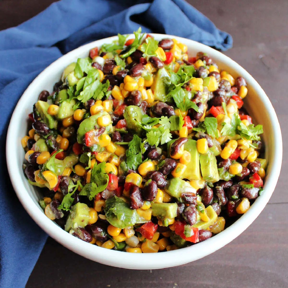 White serving bowl filled with black bean salsa with corn, red pepper, avocado and herbs.