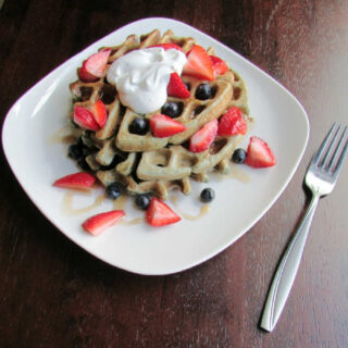 Stack of blueberry sourdough waffles topped with fresh blueberries, strawberries, maple syrup, and whipped cream, ready to eat.