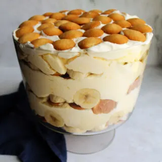 Glass trifle bowl filled with layers of banana pudding with vanilla wafers, sliced bananas and creamy pudding mixture.