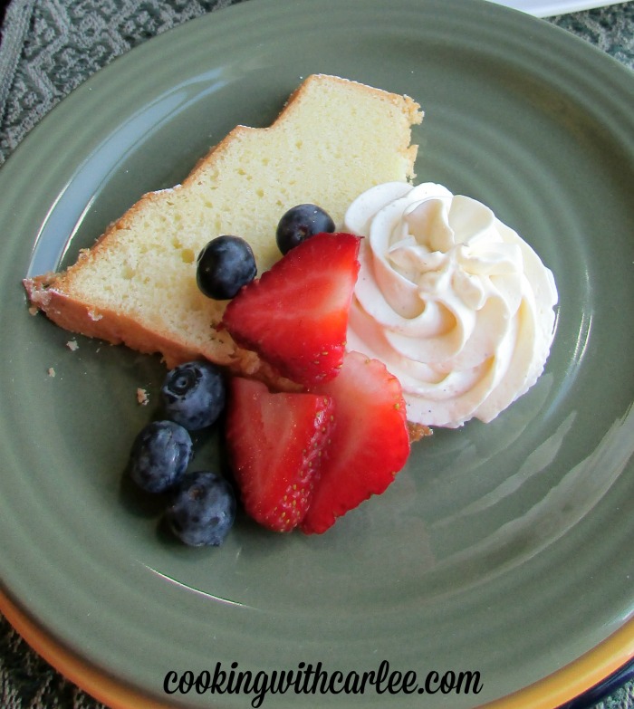 close up of slice of cake with berries and swirl of cream cheese whipped cream.