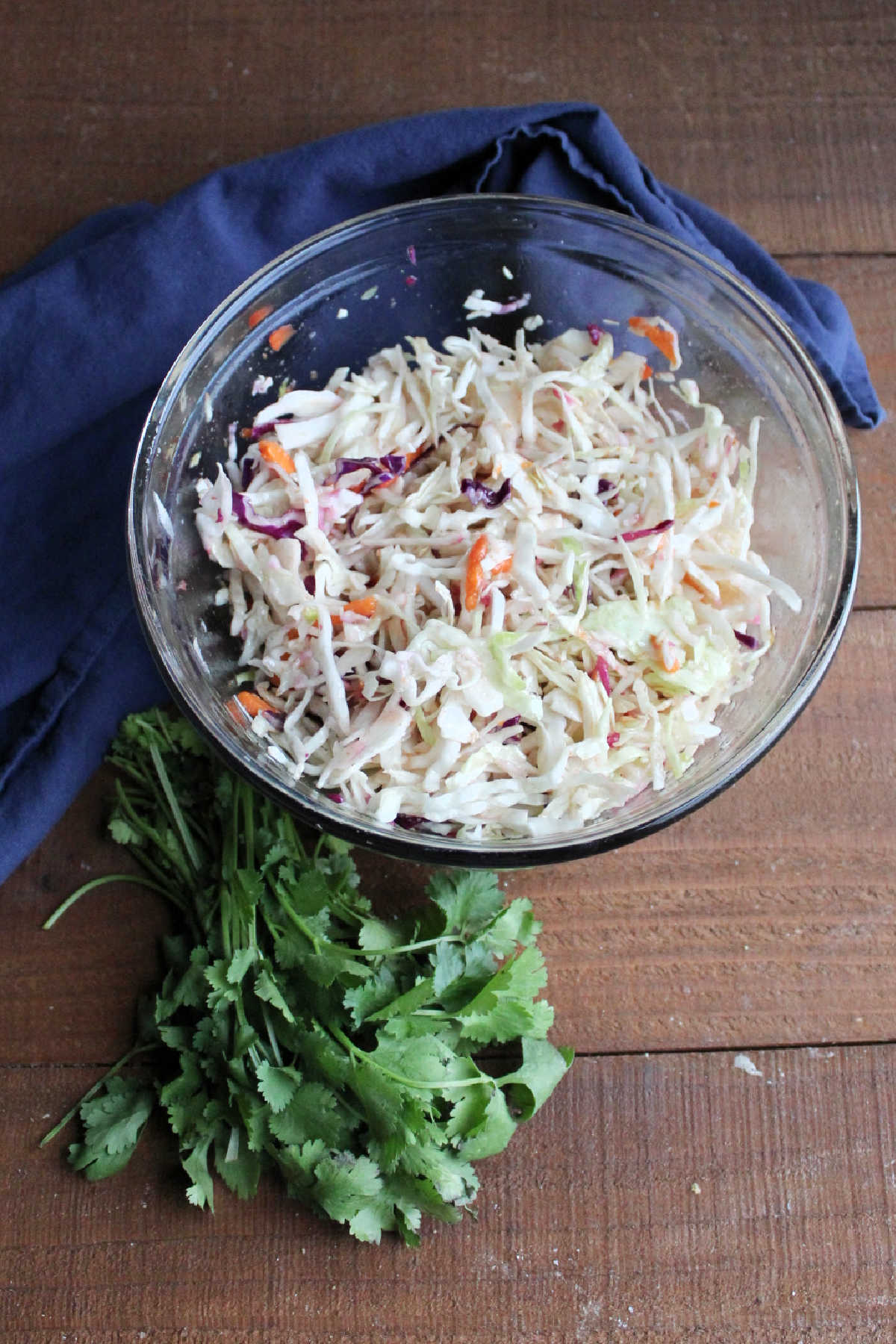 Bowl of dressed coleslaw next to a bunch of fresh cilantro.