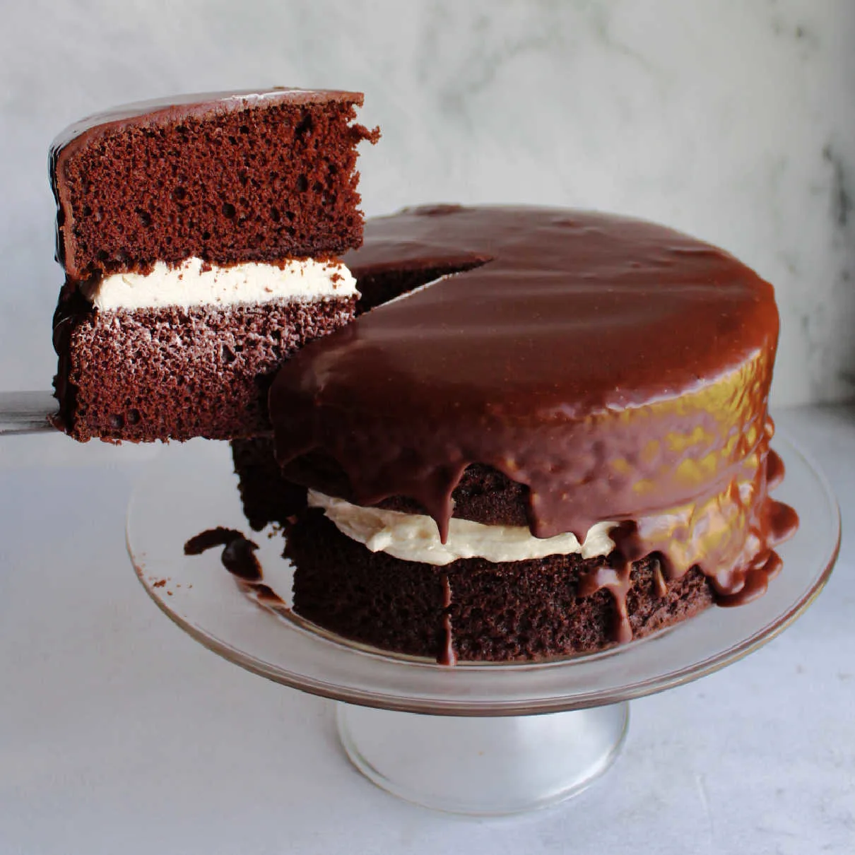 Lifting slice of ding dong cake out of cake, showing chocolate cake layers, creamy vanilla filling and dark chocolate icing.