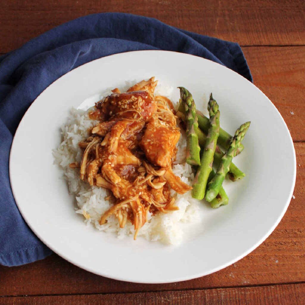 Dinner plate filled with roasted asparagus spears and slow cooker sesame chicken over rice. 