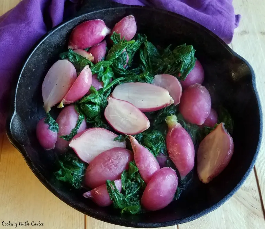 Close up of cast iron pan filled with roasted radish halves and wilted radish greens.