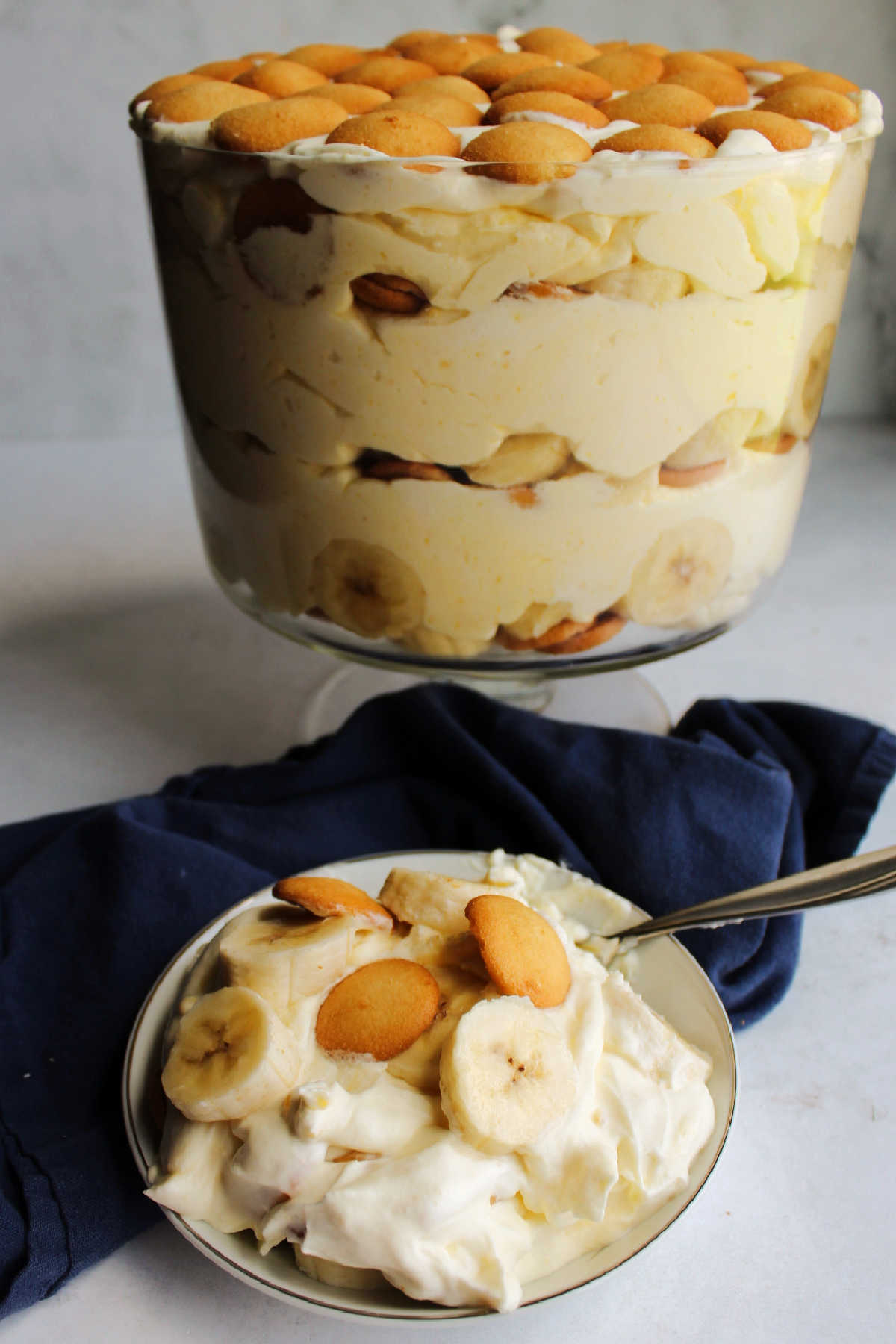 Serving of creamy banana pudding in bowl with remaining pudding in trifle bowl in the background.