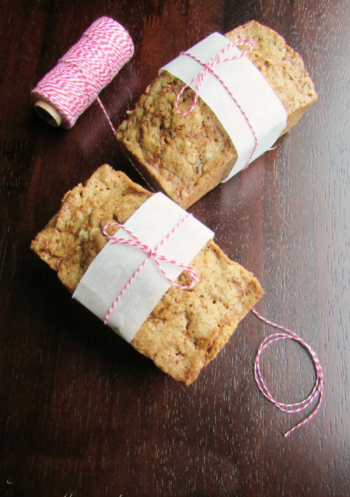Tying bakers twine and a strip of parchment paper around two mini loaves of zucchini bread, getting them ready to give away.